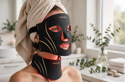 Woman wearing the Solaara Glow Mask and neck piece with red light on, hair wrapped in a towel in a bright spa bathroom